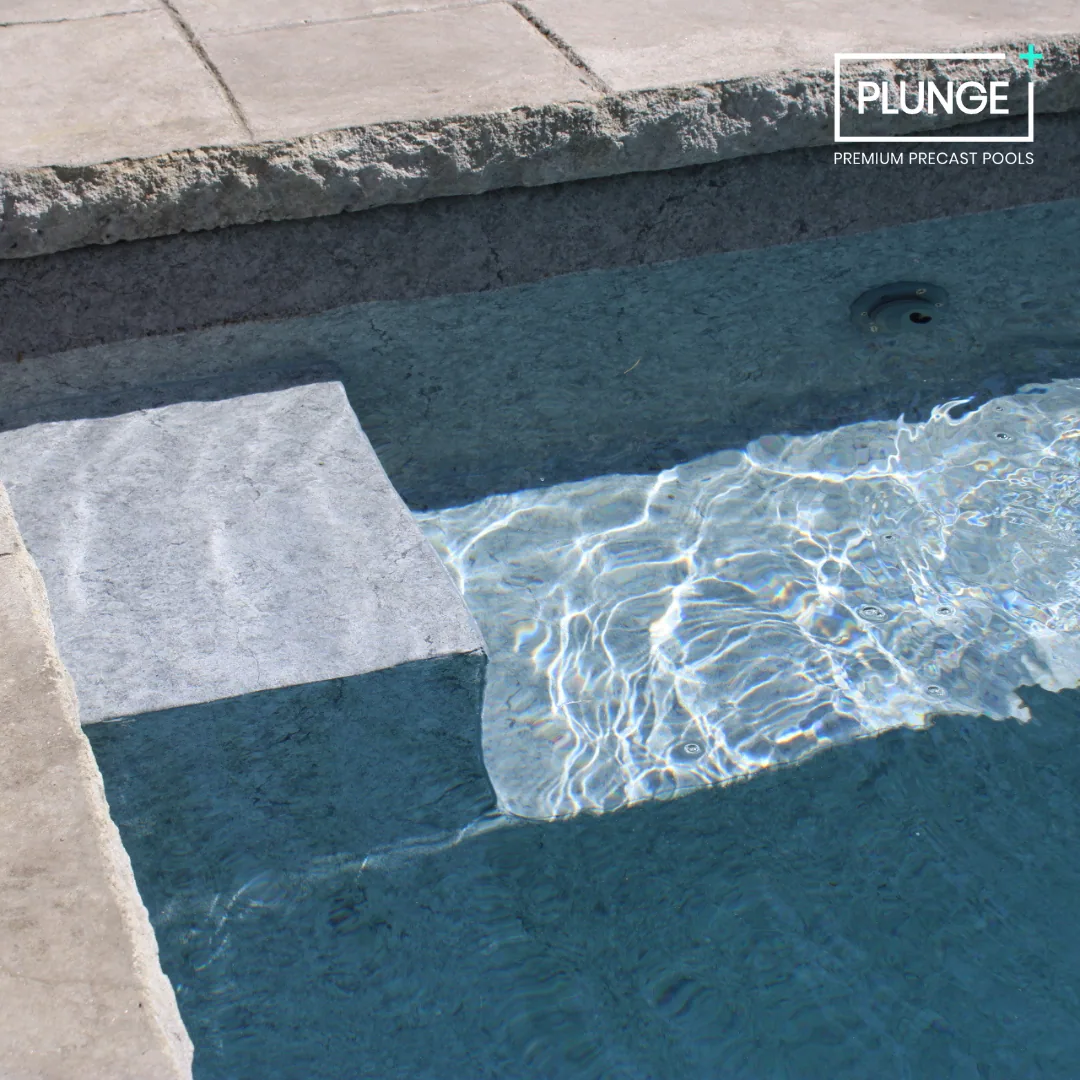Close-up view of an in-ground swimming pool with a stone edge, showing the water and part of the pool wall and steps.