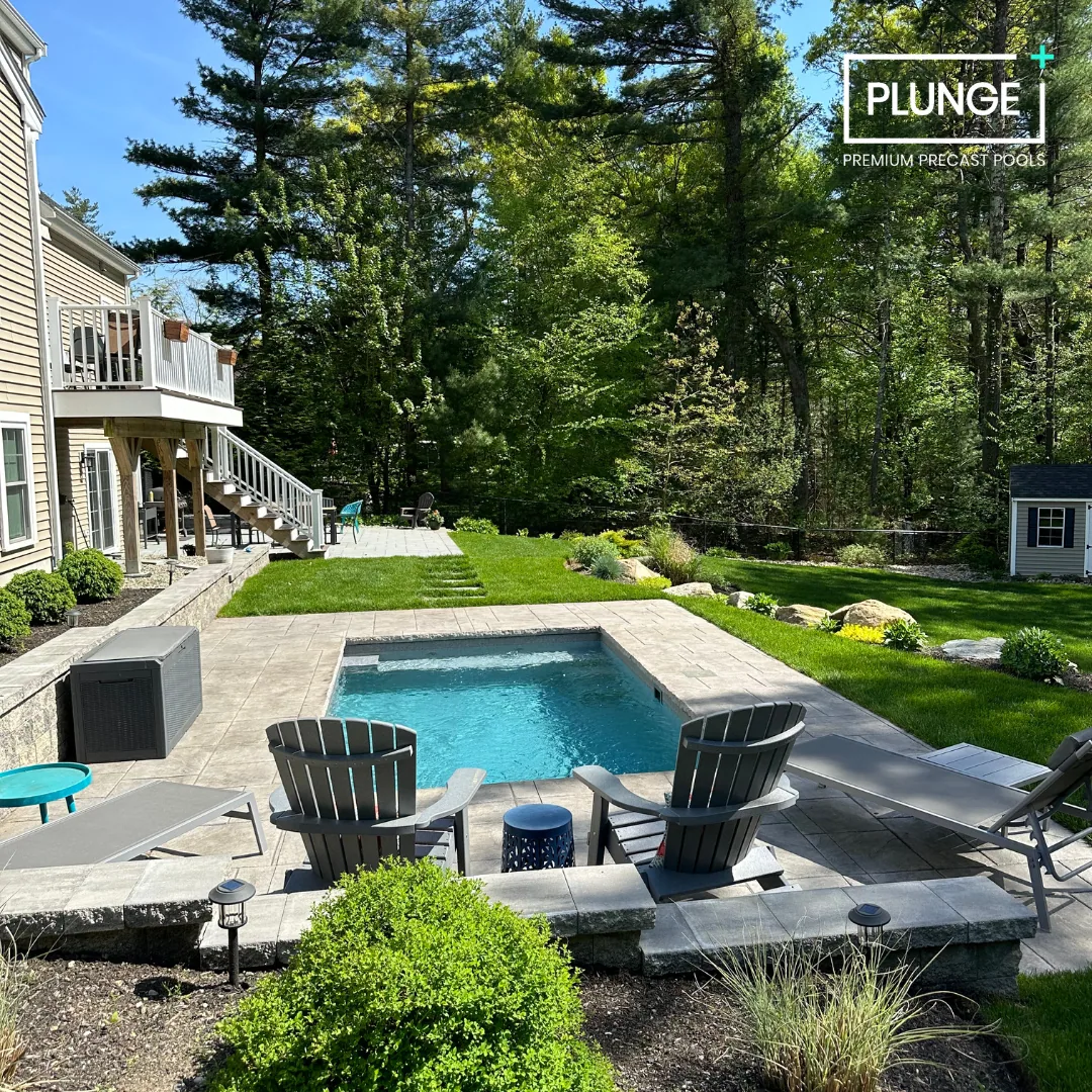Backyard with a small rectangular pool, surrounding patio, lawn, and trees in the background. There is outdoor furniture, including Adirondack chairs, lounge chairs, and small tables.