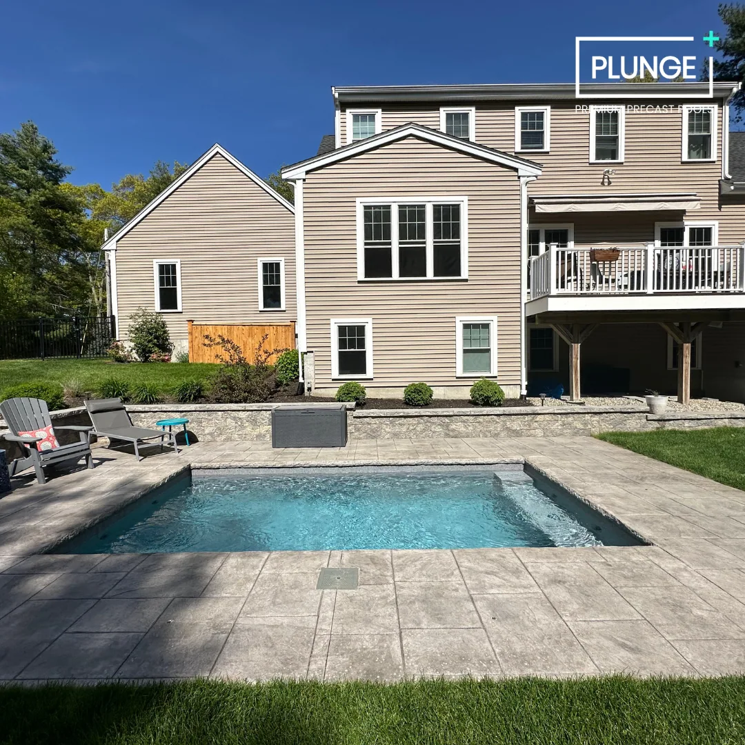 Backyard with a swimming pool, patio furniture, shrubs, and a multi-story house with beige siding and white trim.