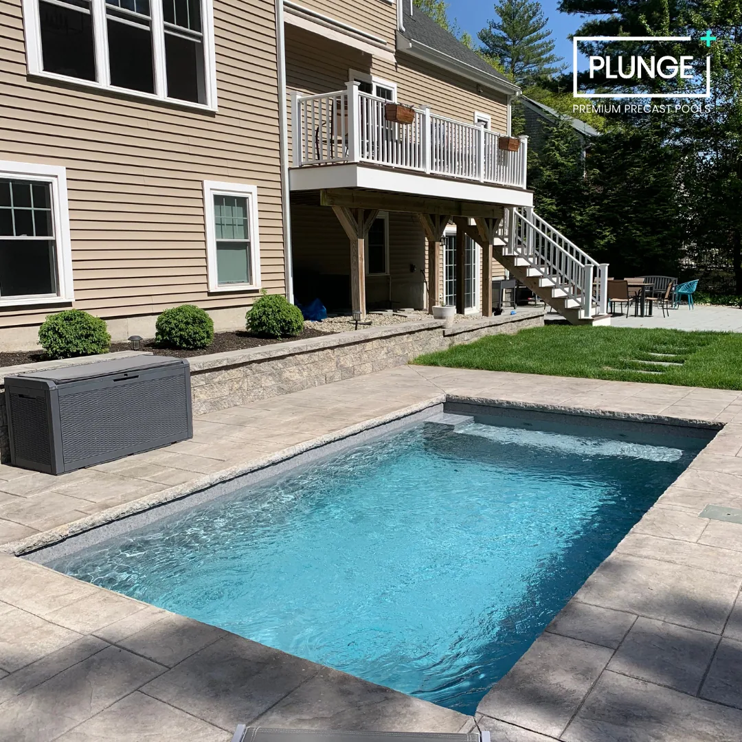 Backyard with in-ground pool, stone patio, beige house with white trim, wooden deck with stairs, outdoor seating area, and green lawn.