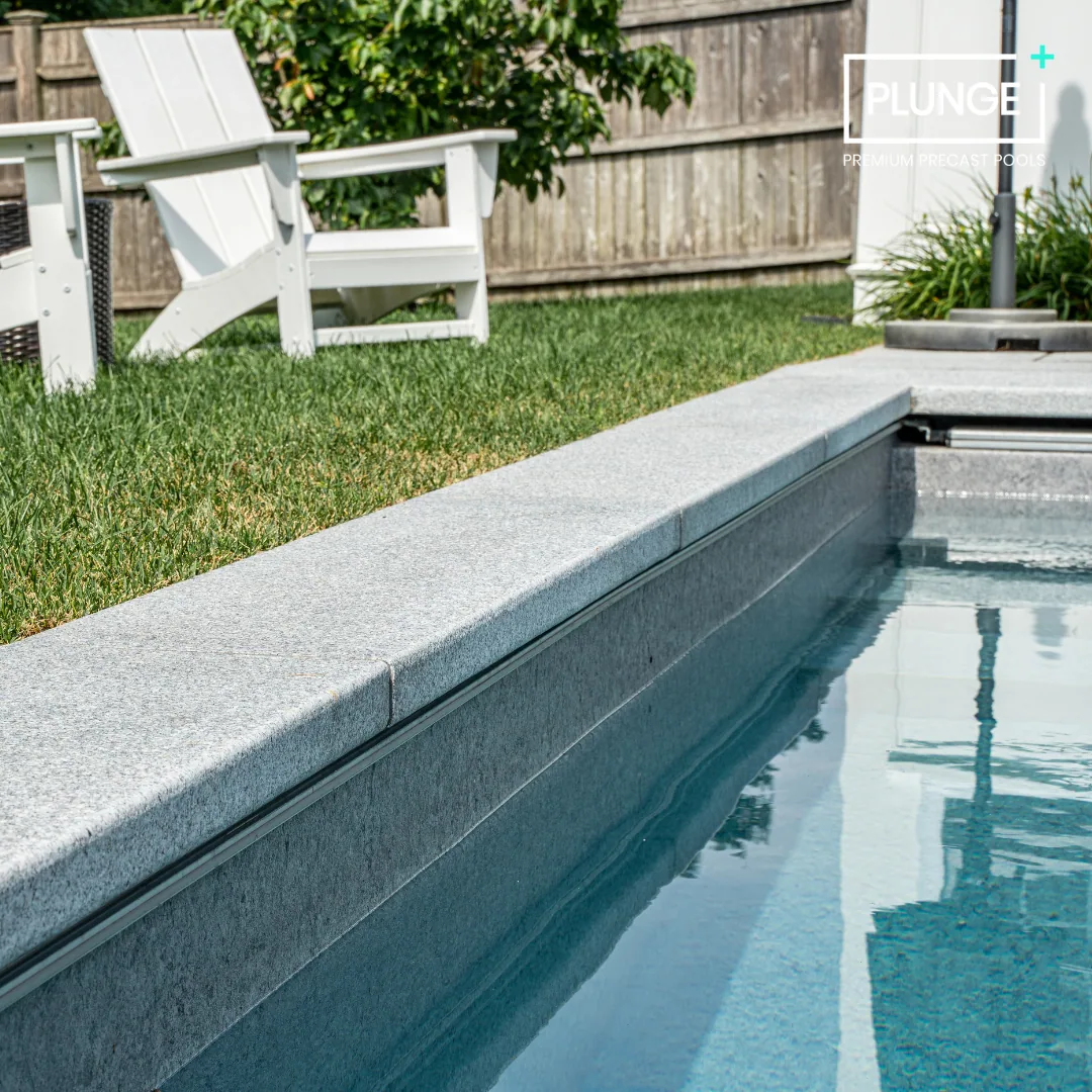 A private backyard with a concrete pool, white pool lounge chairs, green grass, and a wooden fence.