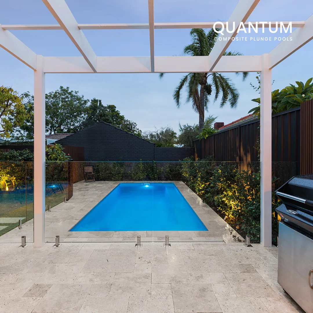 A backyard with a modern swimming pool, a white pergola, and lush greenery, illuminated with decorative lighting, during dusk.