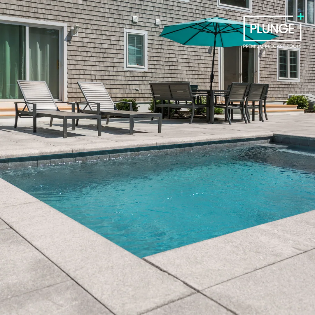 A backyard with a swimming pool, two lounge chairs, a dining table with six chairs, and an umbrella, with a house's outside wall and windows in the background.