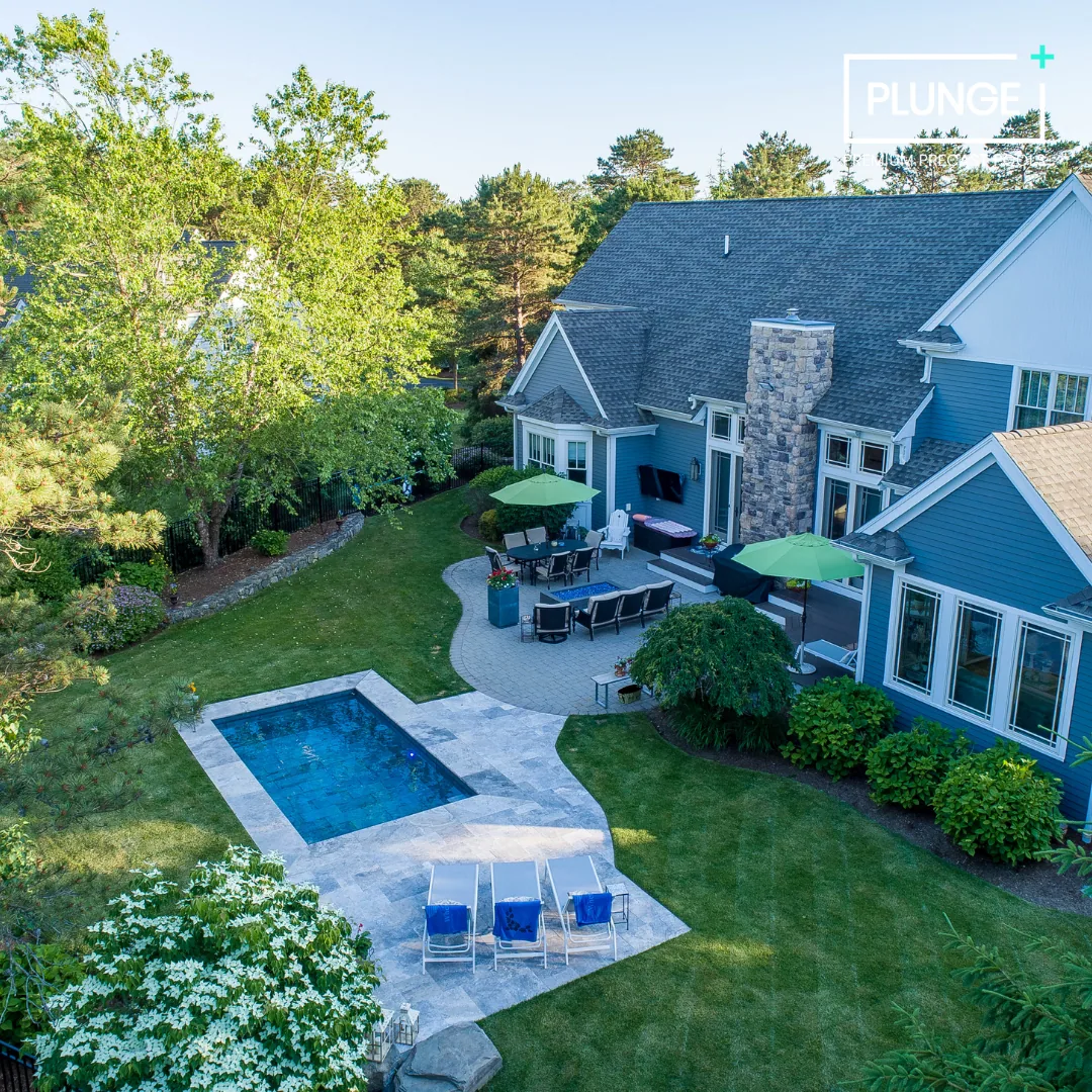 A backyard with a swimming pool, outdoor seating area with umbrellas, and a house with blue siding and multiple windows.