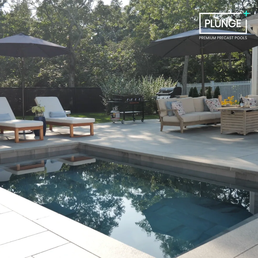 Backyard with a pool, lounge chairs with umbrellas, a sofa set, barbecue grill, and outdoor dining table under sunny sky.