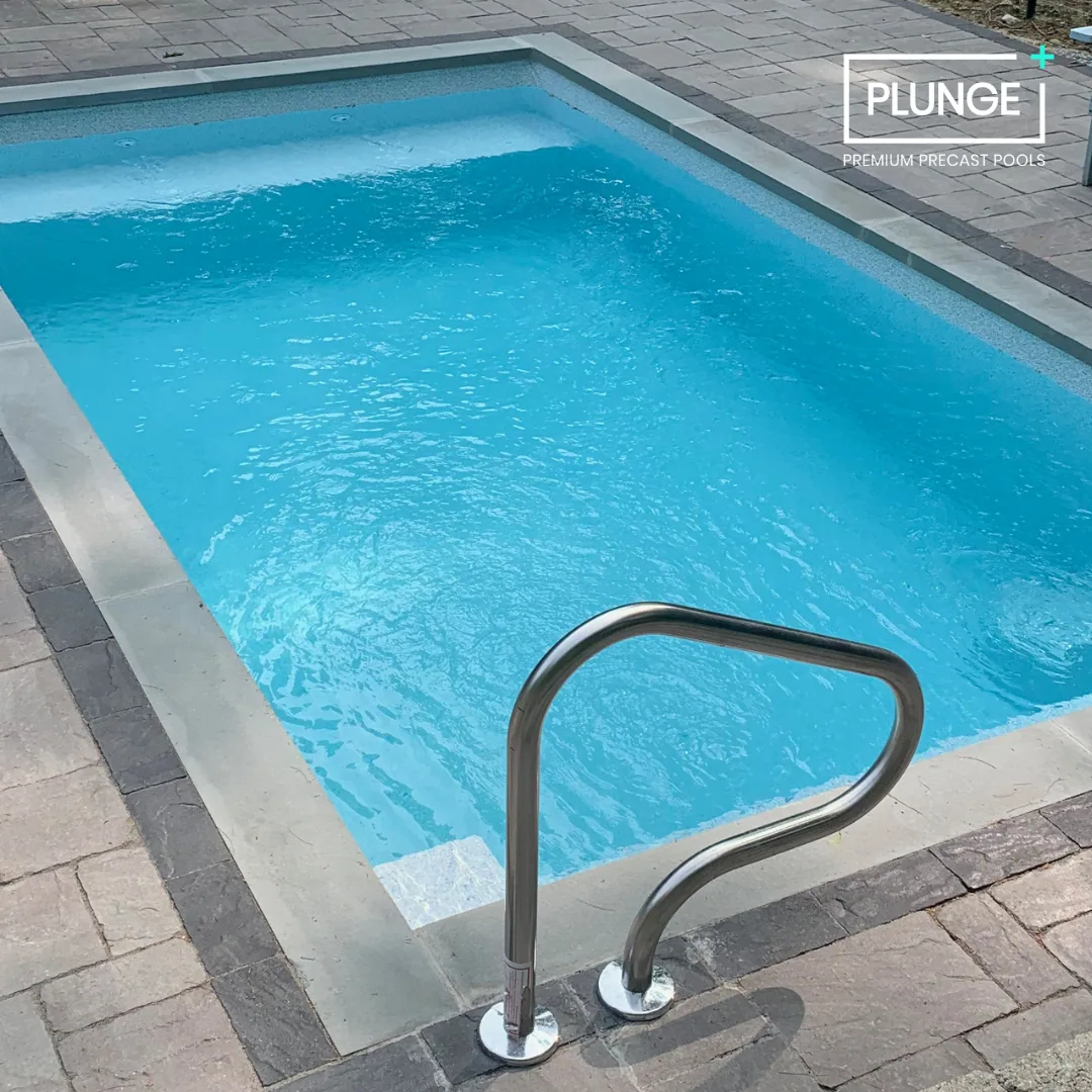 A small rectangular pool with blue water, surrounded by a stone deck, with a metal ladder at the front.