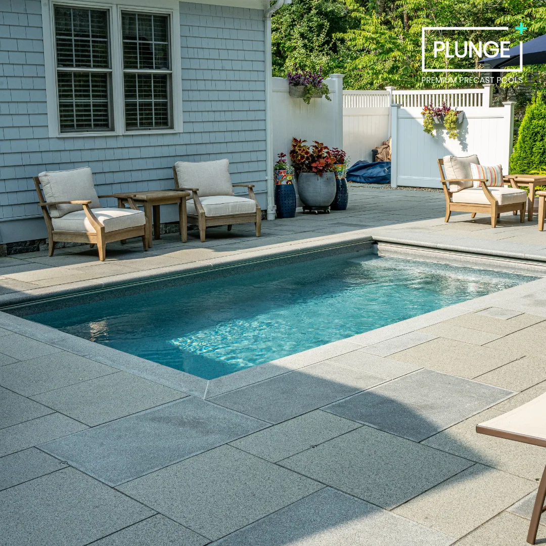 A backyard with a small swimming pool, outdoor lounge chairs, potted plants, and a white privacy fence.