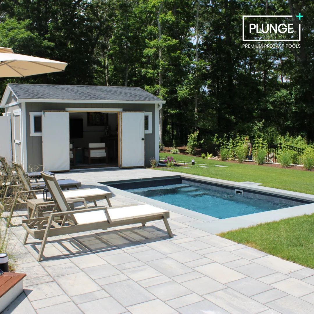 Backyard with a rectangular pool, poolside lounge chairs, a small shed with double doors, and a grassy area bordered by trees and plants.