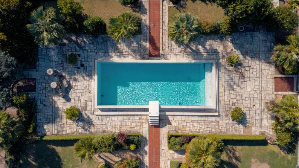 Rectangular inground pool seen from above, surrounded by a stone deck and landscaping