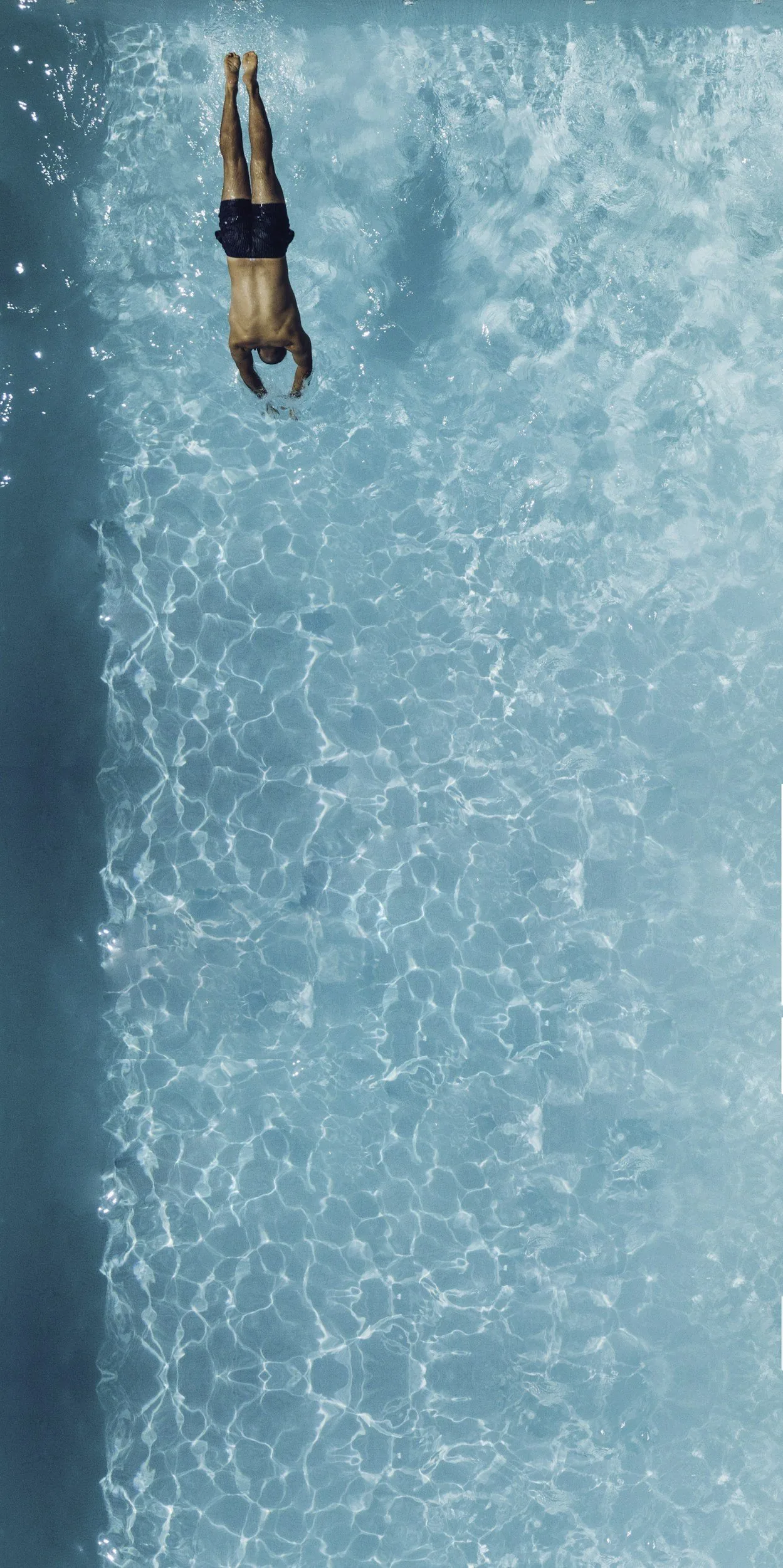 A person diving into a clear blue swimming pool, captured from above, with rippling water.